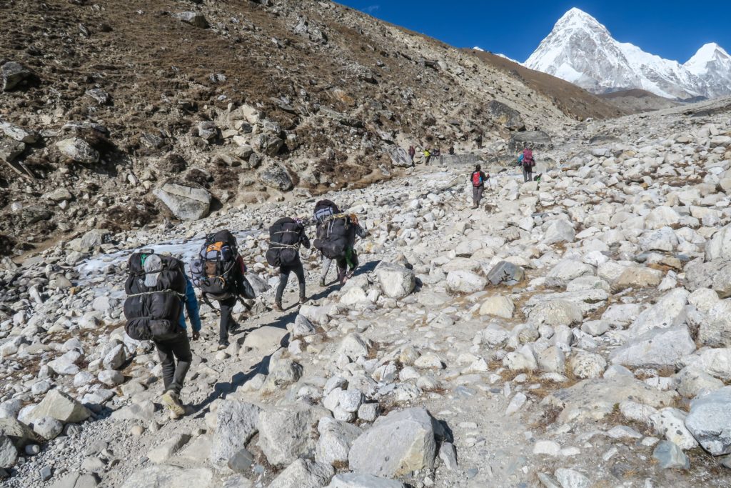 Climbing party of seven individuals traversing rocky path with large snow capped mountains in the distance