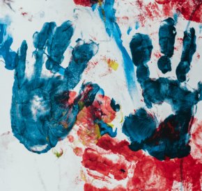 Blue handprints on a finger painted multicolored canvas
