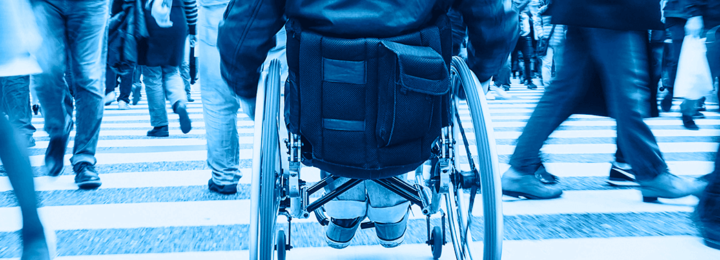 ground level view of a wheelchair user crossing a busy crosswalk filled with others