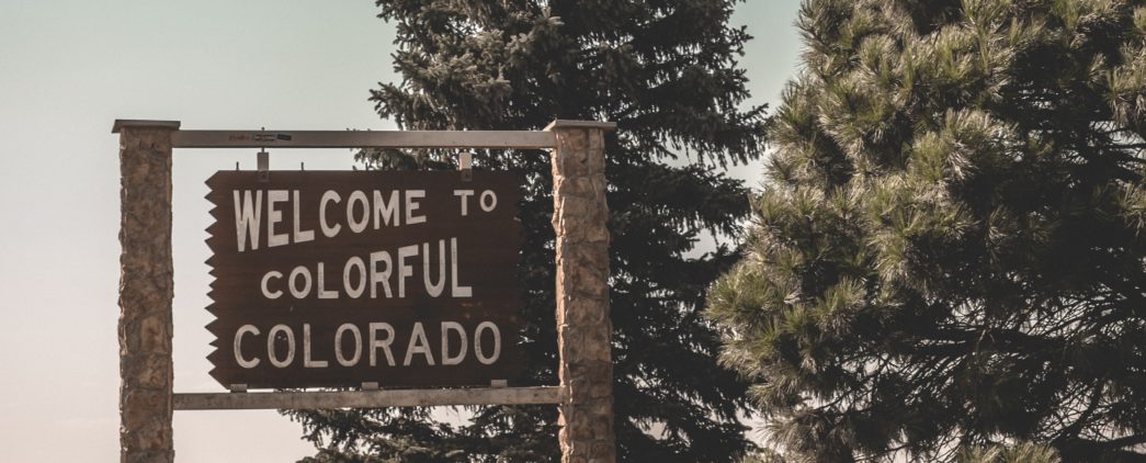 Sign that says 'welcome to colorful Colorado' next to two trees