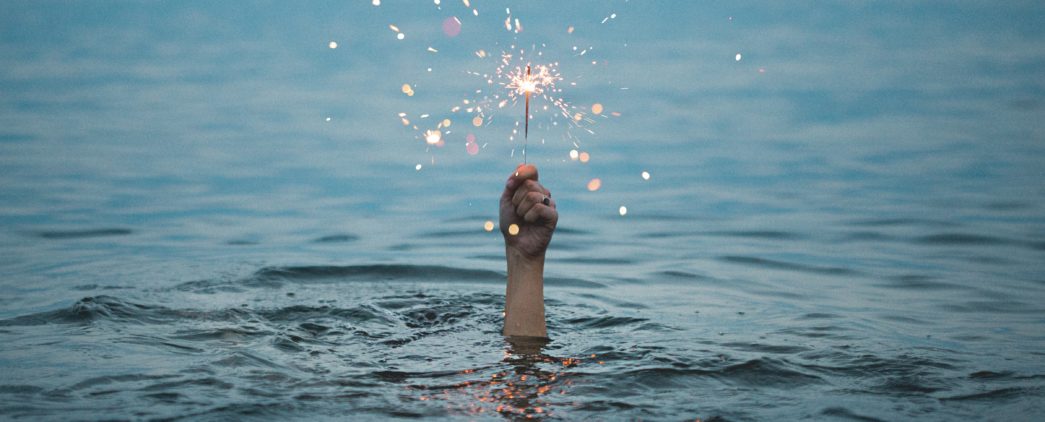 hand reaching out of the water holding a sparkler