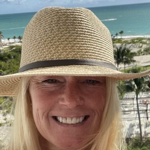 Heather Schiffbauer Headshot of her with a broad brimmed hat with blond hair in a beach setting background