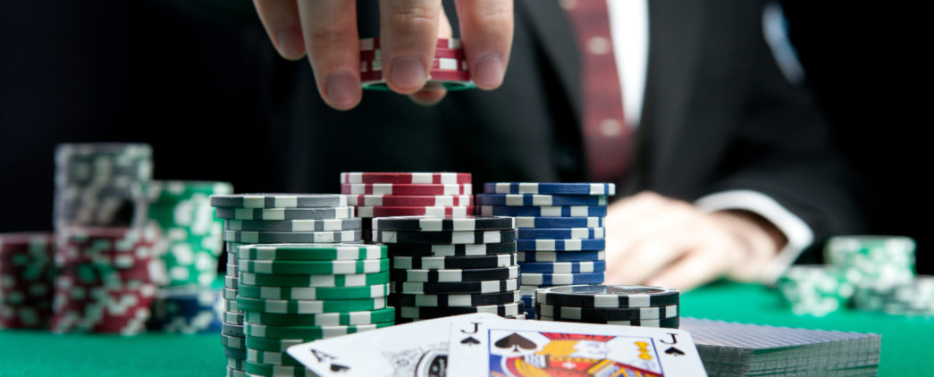 A man in a suit reaches for poker chips over a set of cards.