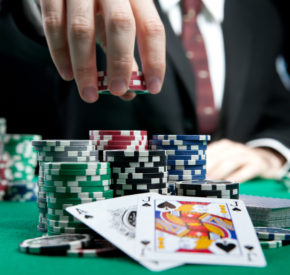 A man in a suit reaches for poker chips over a set of cards.