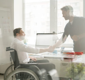 Businessman shaking hands with man in wheelchair behind the window at office