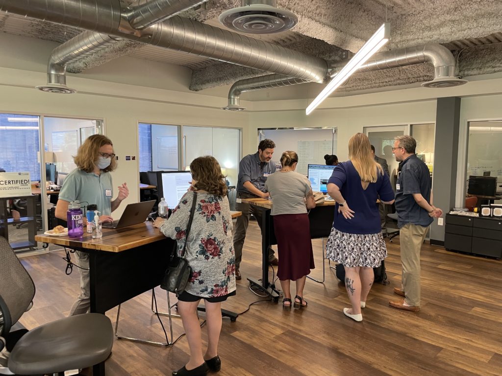 Crowds gather around the demonstration desks, eager to learn more about digital accessibility. 