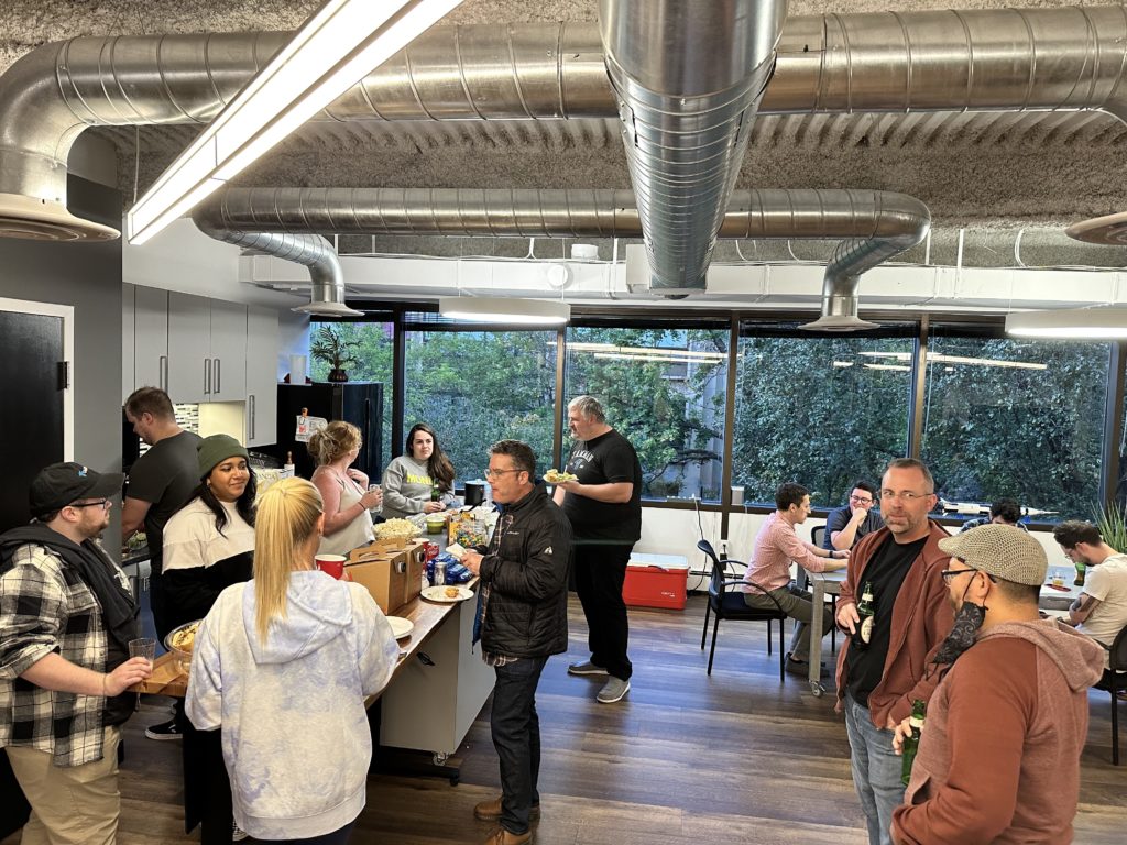 A large group of Tamman employees hangout in the office while enjoying food and drinks.