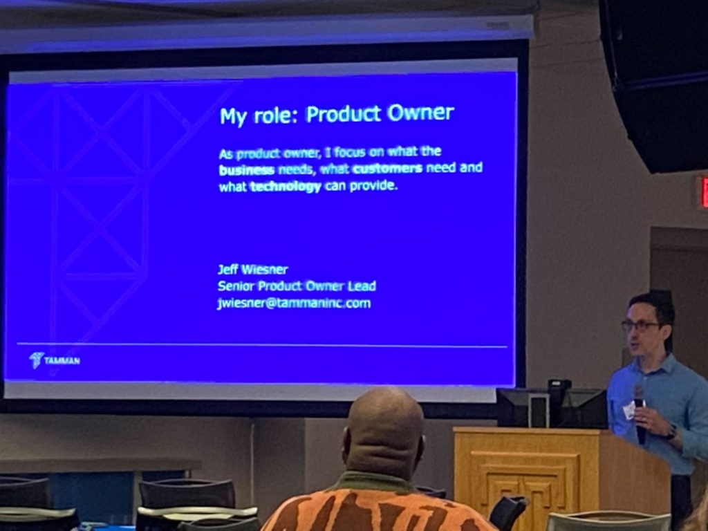 Jeff stands behind a podium and delivers a slide that describes his role as a Product Owner at Tamman.