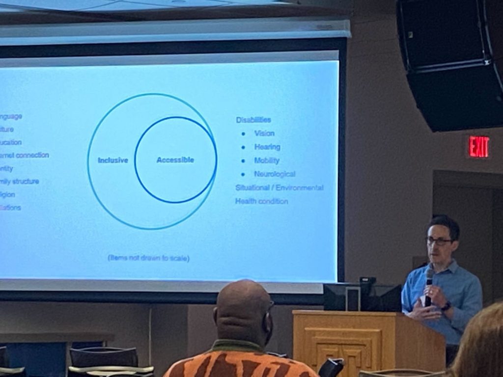Jeff stands behind a podium and delivers a slide that features a Venn Diagram that focuses on the difference between inclusive and accessible design.