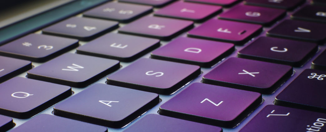 A close up of a laptop keyboard with the pink and green colors from the screen reflecting off of the keys.