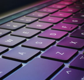 A close up of a laptop keyboard with the pink and green colors from the screen reflecting off of the keys.