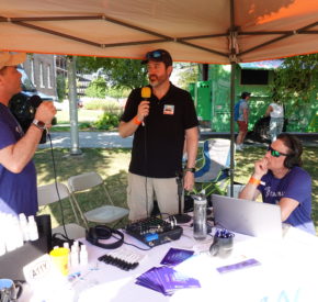 Marty Molloy, Mike Mangos, and Markus Goldman gather at a table covered in audio equipment under a canopy to record a podcast.
