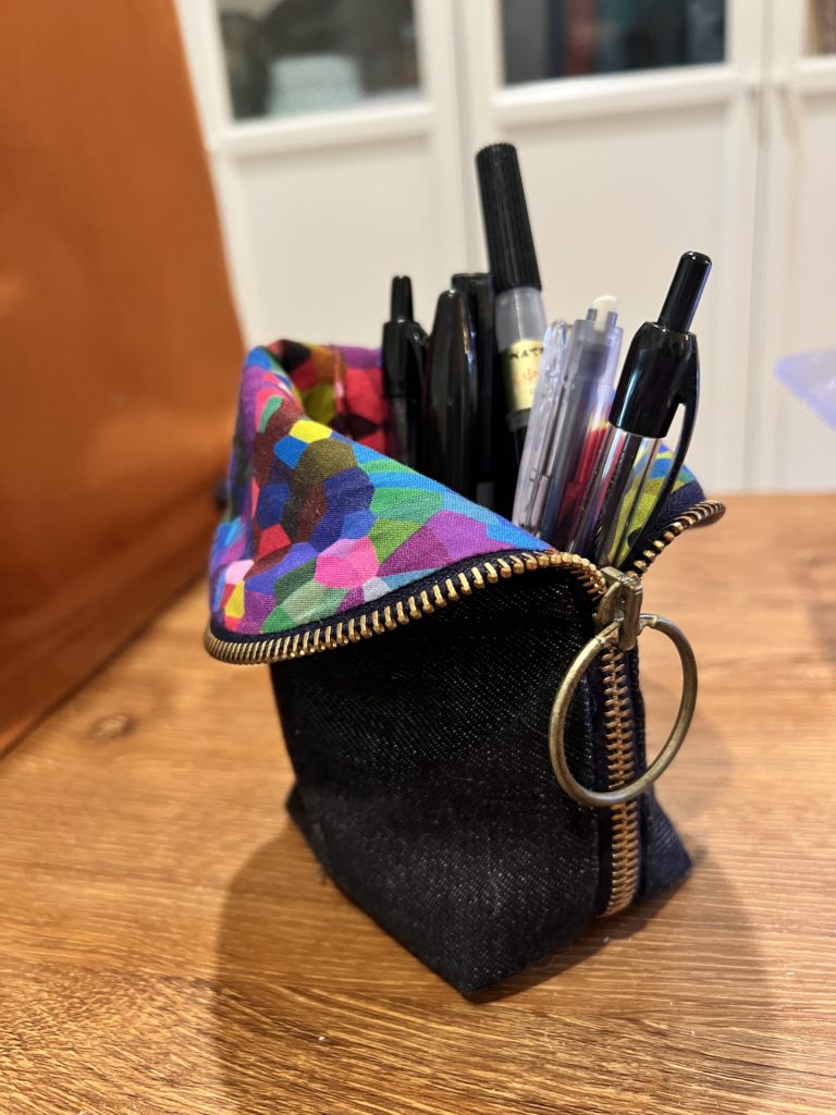 A hand-made multi-colored pencil case, with multiple pens inside.