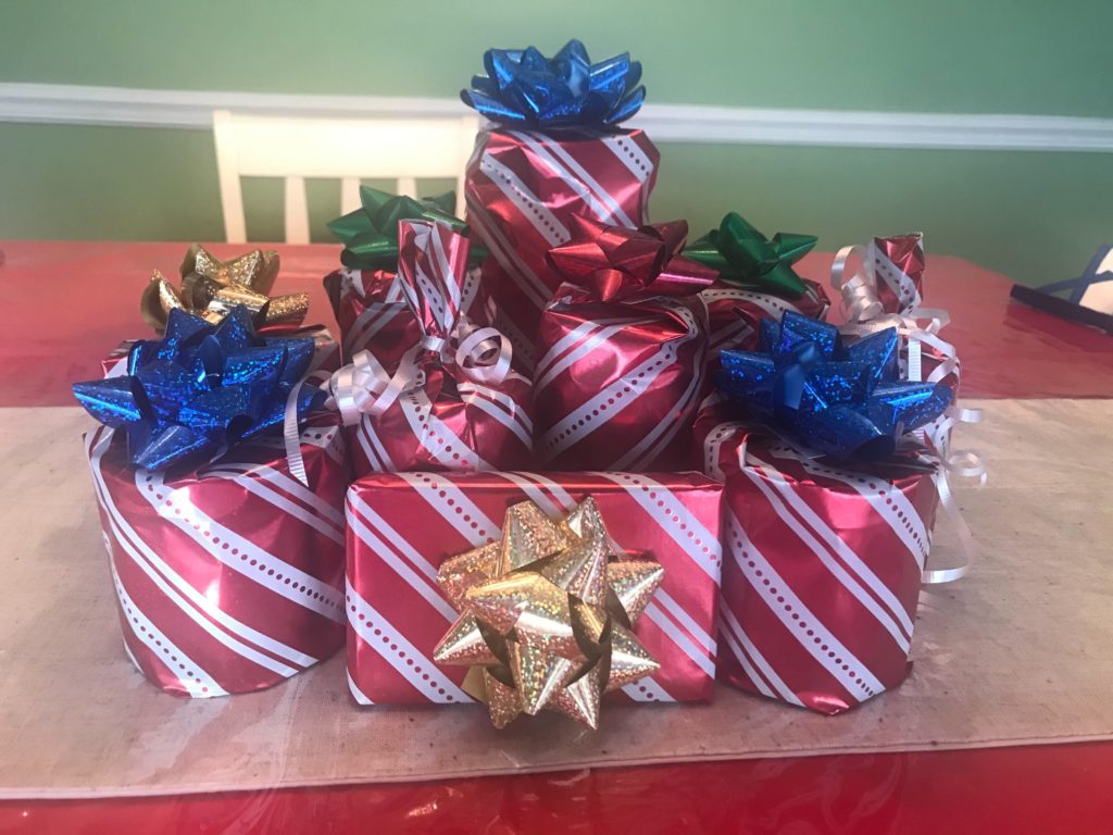 A pile of gifts covered in red and white wrapping paper. On top of the gifts are white ribbons and multi-colored bows.