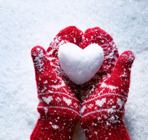 Red mittens holding a heart-shaped snowball on a snowy day.