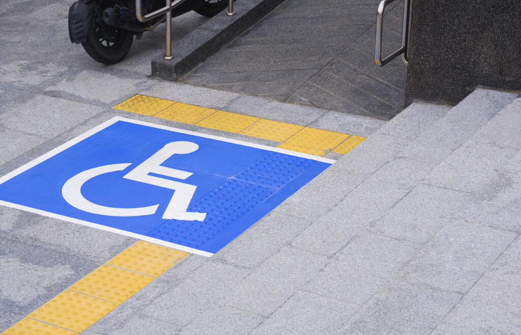 Disabled wheelchair sign with a ramp and yellow tactile paving lines on different levels of marble pavement surfaces with stairs in the public area, which illustrates the need for color contrast in everyday life.