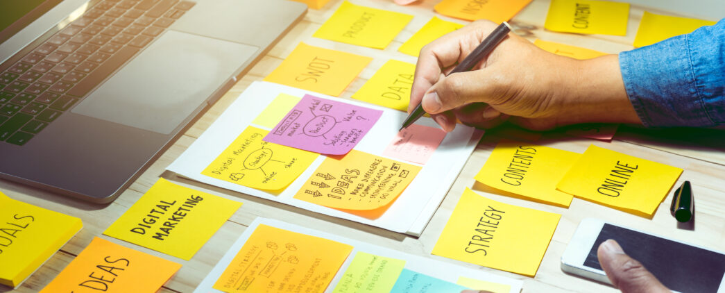 Digital marketing professional brainstorms his technical project goals on sticky notes spread across his desk. The sticky notes cover digital marketing strategy, communication ideas, online content, and other digital marketing needs.