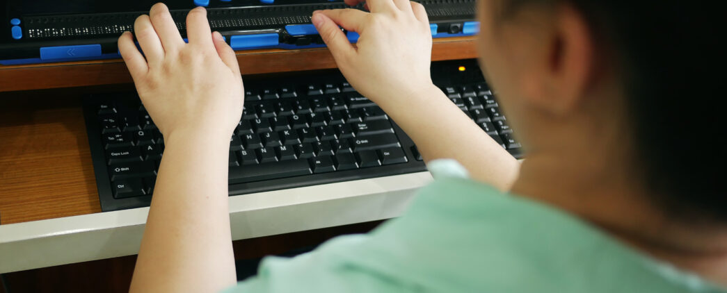 Rear view of person with blindness disability using computer keyboard and braille display or braille terminal a technology assistive device for persons with visual impairment