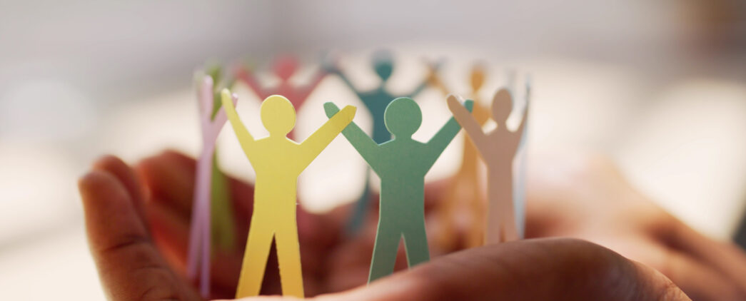 Alt Text: Hands holding a colorful circle of paper cutouts shaped like people, symbolizing community, inclusivity, and support