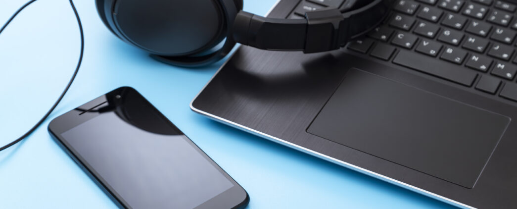 Close-up of a smartphone, over-ear headphones, and a laptop on a bright blue background to represent a screen reader